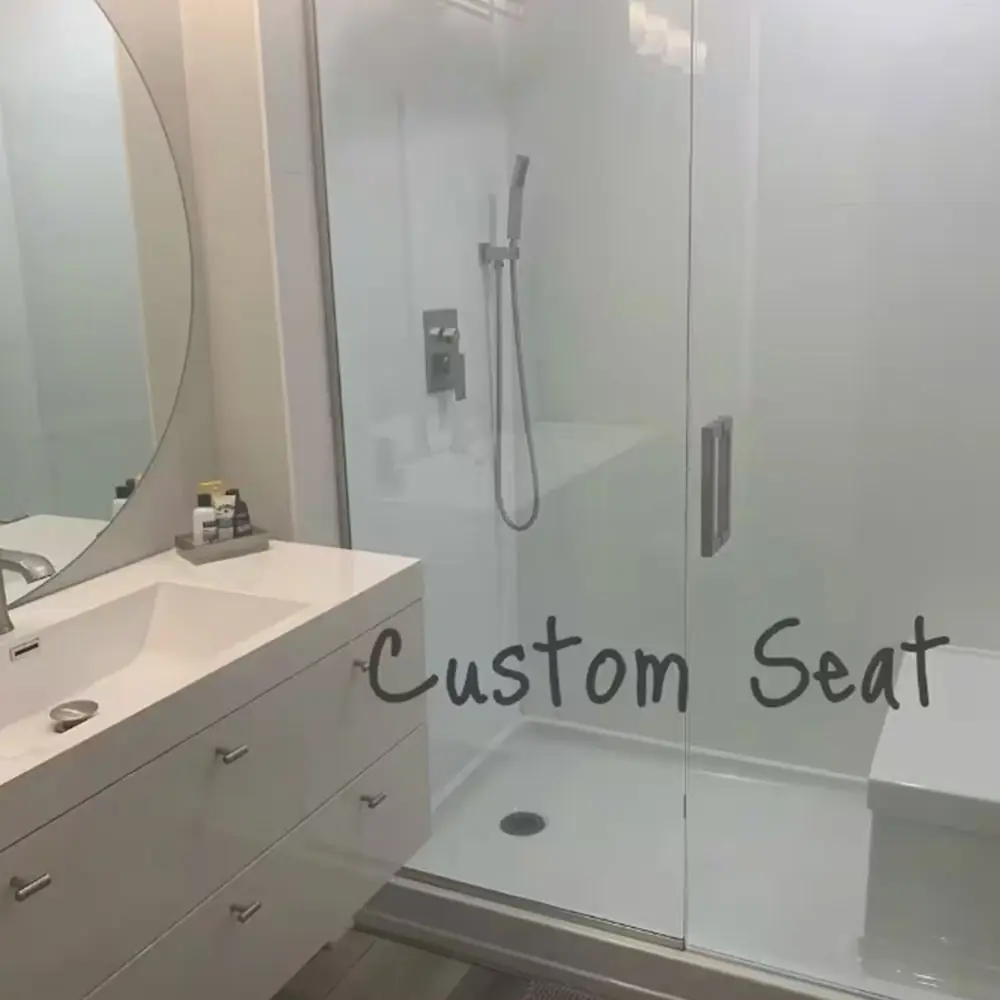 Modern bathroom with a white vanity and sink on the left, round mirror above, and a glass-enclosed shower on the right featuring a built-in custom seat. The words “Custom Seat” are written on the shower glass.